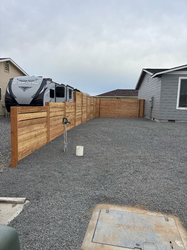 Horizontal wood slat fence along L-shaped yard with gravel
